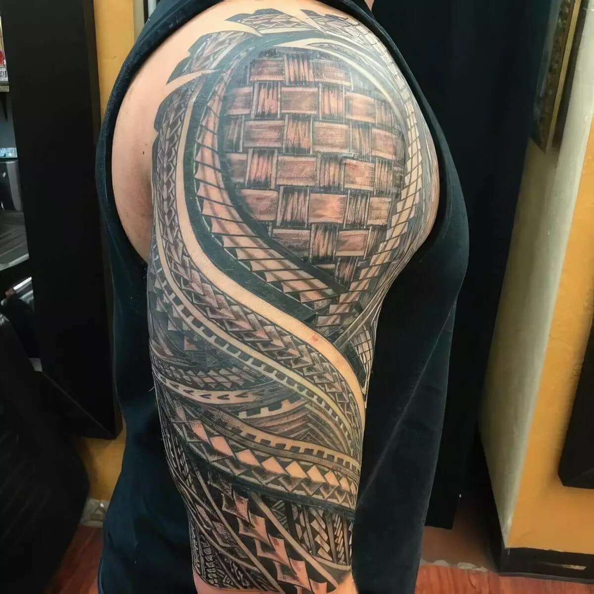 Person with an elaborate Polynesian-style tattoo sleeve covering their right upper arm and shoulder. The tattoo features intricate patterns, including geometric shapes and weaving designs.