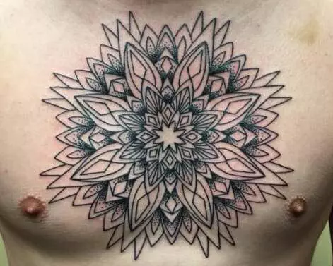 A symmetrical, intricate mandala-style tattoo spans the center of a person's chest, featuring detailed geometric and floral patterns in black ink.