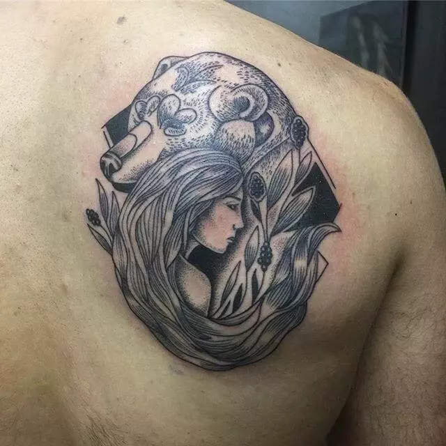 Tattoo on upper back features a design of a woman with flowing hair surrounded by leaves and berries, with a bear's head in the background.