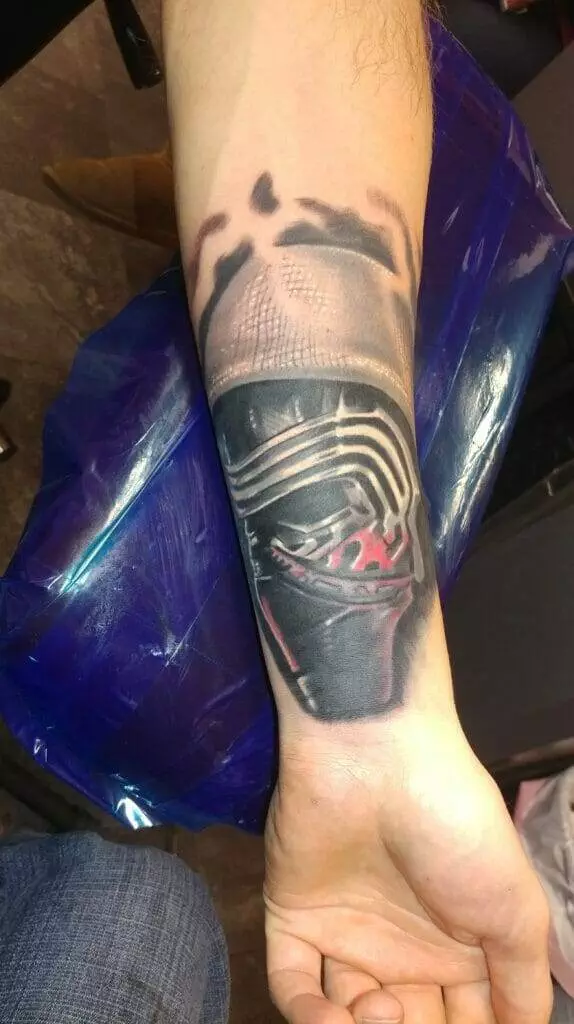 A forearm tattoo depicting a character in a helmet, with intricate design work and shading.