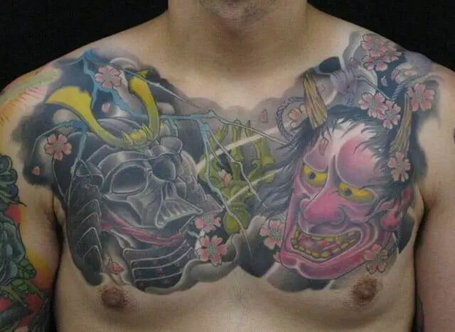 A man's chest tattoo featuring a samurai helmet and a red-faced oni mask with surrounding pink flowers and branches.