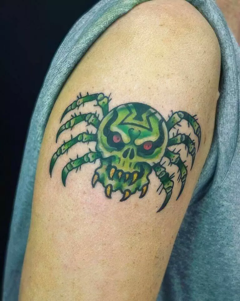 A green spider with a skull face tattooed on an upper arm. The person is wearing a sleeveless gray shirt.