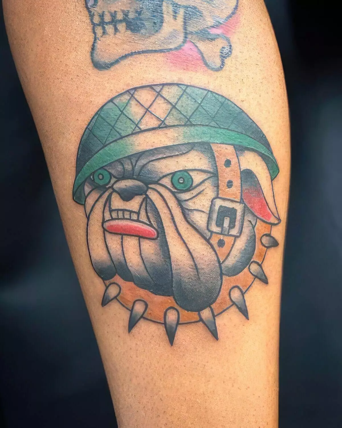 A colorful tattoo of an angry bulldog wearing a green helmet with spikes on its collar, inked on a person's arm.