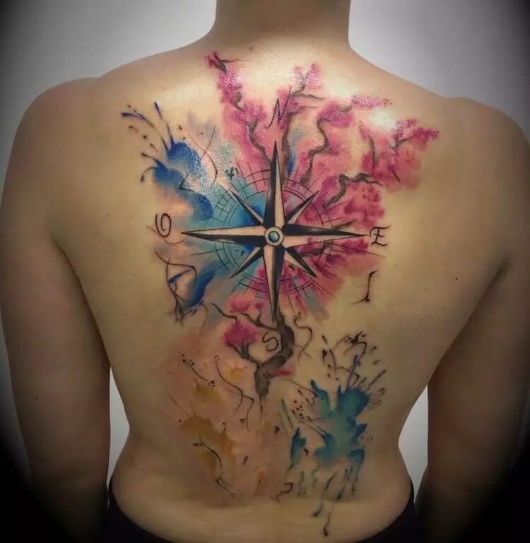 A person with a large, colorful back tattoo of a compass surrounded by abstract watercolor designs in blue, pink, and orange hues.