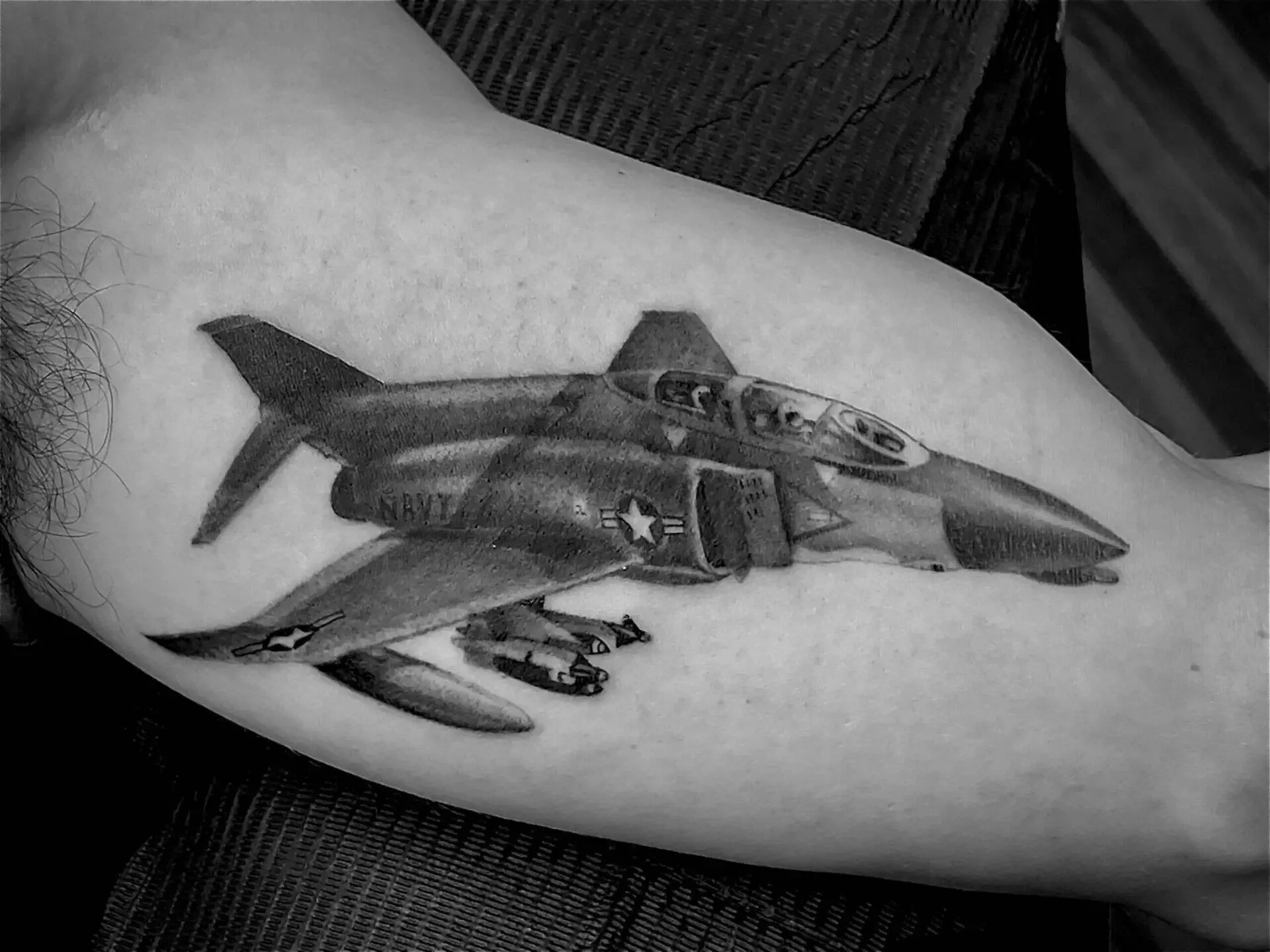 A black and white tattoo of a military jet with missiles, marked with 