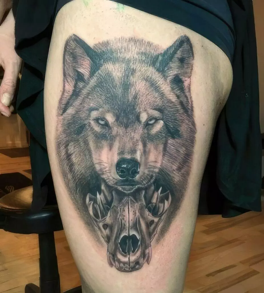 A tattoo on a person's thigh features a wolf's head above a detailed depiction of a wolf's skull.