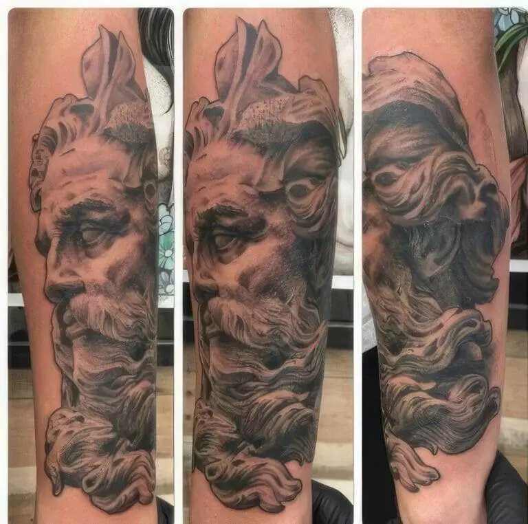 A detailed black and grey tattoo of a classical statue head, depicting a bearded man with flowing hair, on a person's forearm. The tattoo is shown from three different angles.