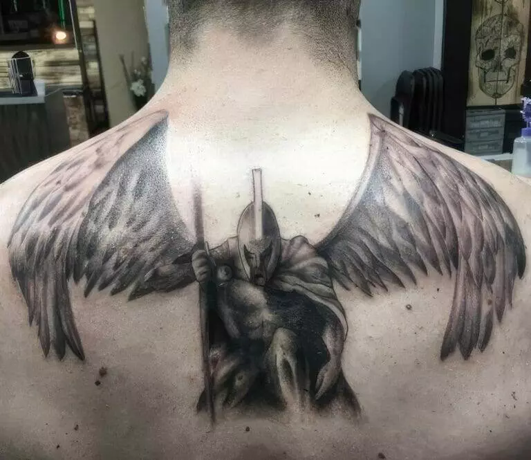 Tattoo of a warrior with a helmet and spear, featuring large wings, covering the upper back.