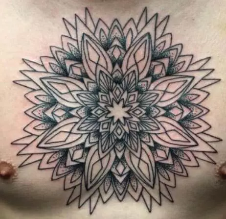 A large, intricate geometric tattoo design with multiple layers of symmetrical shapes is inked on a person's chest, centered between their nipples.