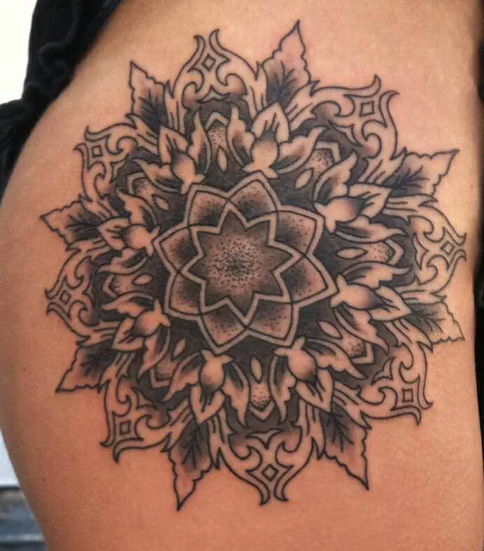 A detailed black ink mandala tattoo on skin, featuring intricate floral and geometric patterns, covers a portion of the side hip area.