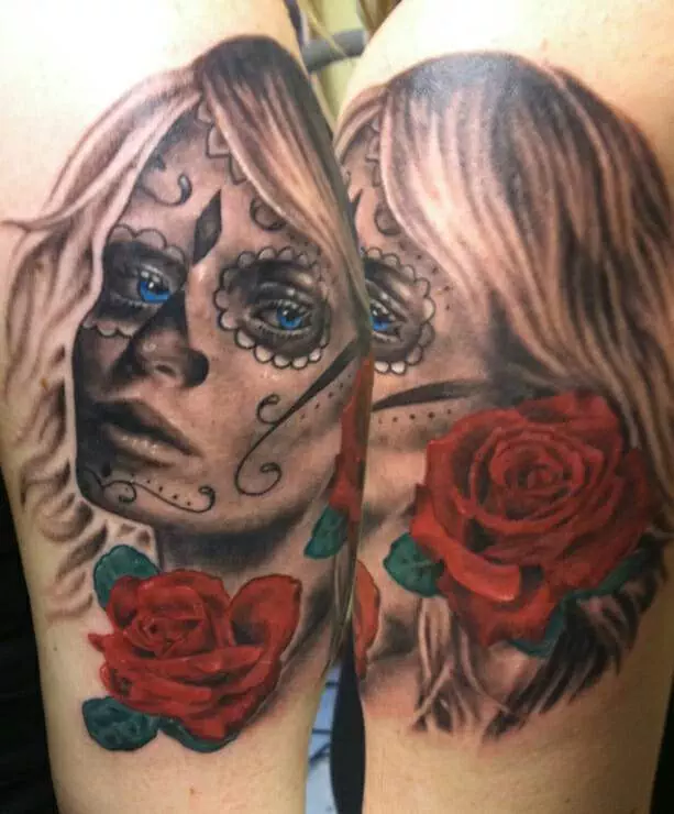 A tattoo depicts a woman's face with facial decorations resembling a sugar skull makeup and a rose beside her.