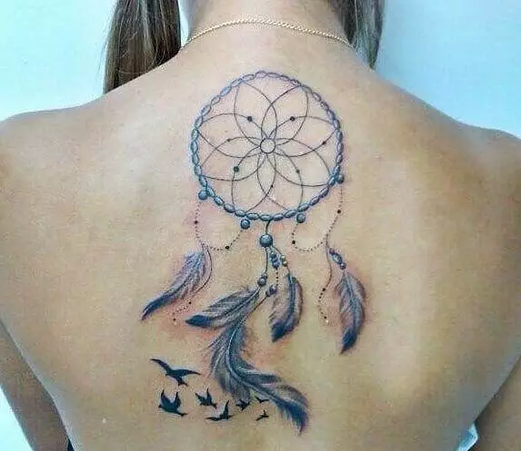 A woman with a tattoo of a dreamcatcher with feathers and birds on her upper back.