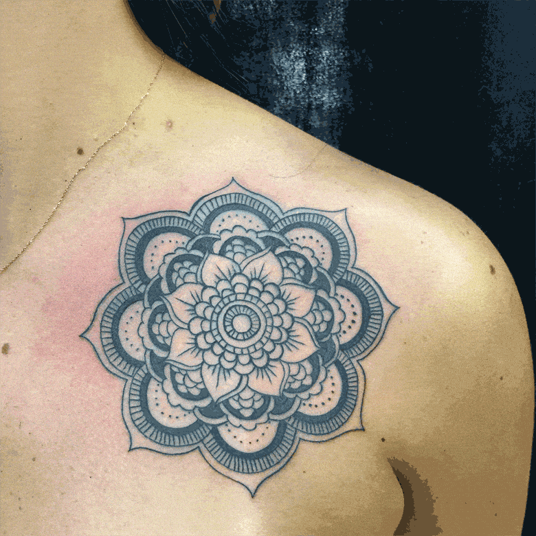 A detailed black and white mandala tattoo is inked on a person's upper back and shoulder area.