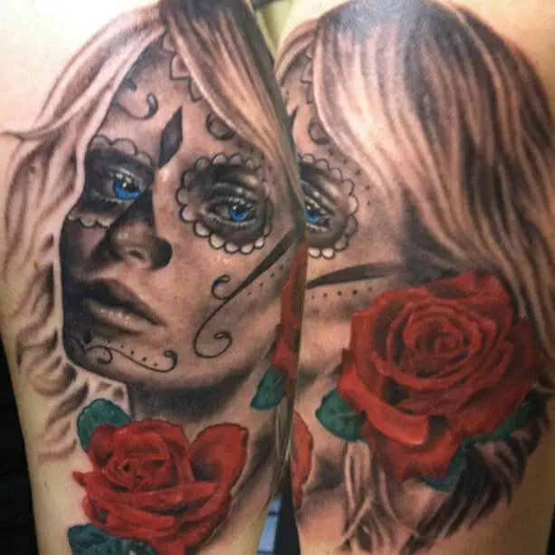 A realistic tattoo on skin depicting a woman's face with sugar skull makeup and red roses.