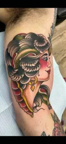 A colorful tattoo of a woman with wavy hair and a snake wrapped around her head, depicted on a person's arm.