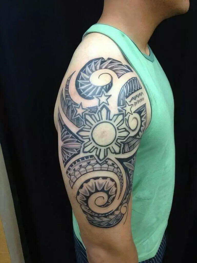 A person wearing a sleeveless green shirt displays a detailed black and gray tribal tattoo on their upper arm, featuring stars and a sun-like design.