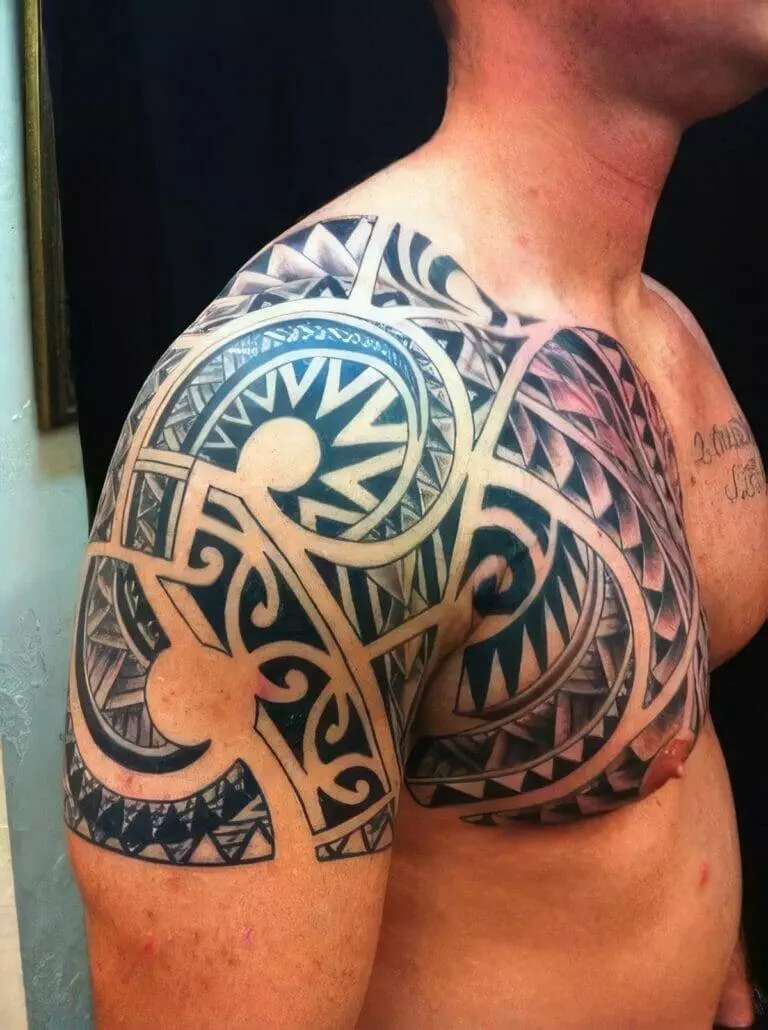 A close-up of a person's upper torso displaying a large, intricate tribal tattoo covering the shoulder, upper arm, and part of the chest in black ink.