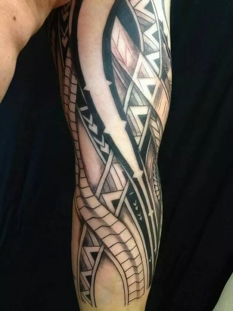 A detailed arm sleeve tattoo with geometric patterns and tribal design elements. The tattoo features a combination of black, grey, and skin-toned areas.