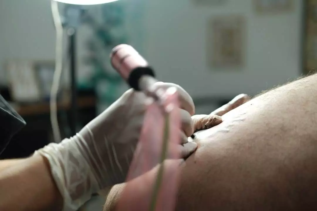 A tattoo artist wearing gloves is tattooing a design on a person's skin using a tattoo machine.