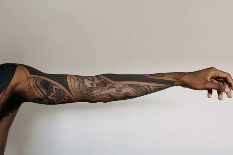 An outstretched arm with intricate geometric and abstract tattoos, set against a plain background.