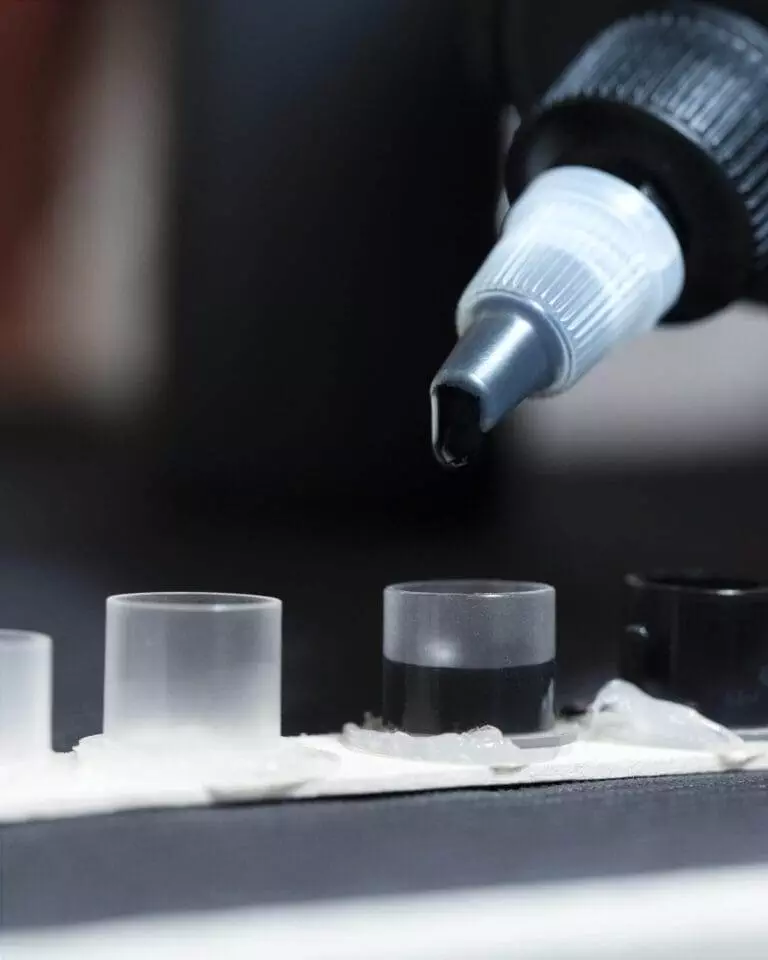 Close-up of a dropper dispensing a liquid into cylindrical containers arranged in a row on a surface.