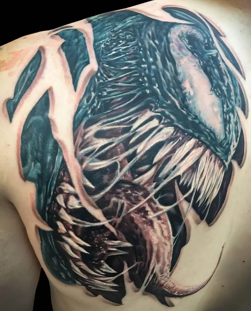 A detailed back tattoo of a monstrous creature with sharp teeth, a large tongue, and a dark, glossy exoskeleton, appearing to tear through the skin.