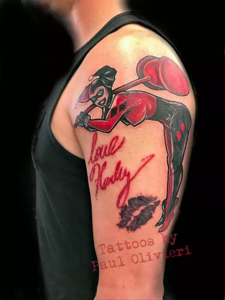 A tattoo on a person's upper arm features Harley Quinn with a hammer, 