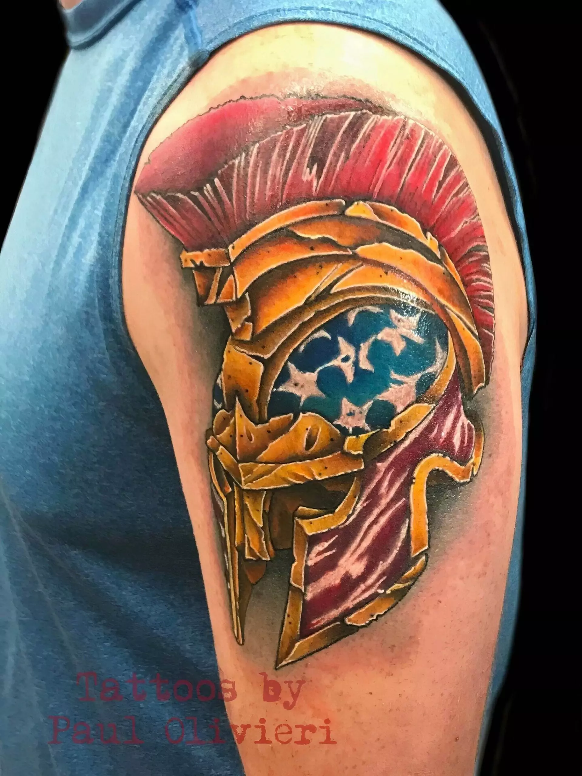 A colorful tattoo of a gladiator helmet with a blue and white star pattern is on an upper arm. The text reads, 