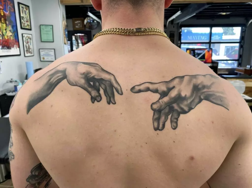 A person's back with tattoos depicting the hands from Michelangelo's 