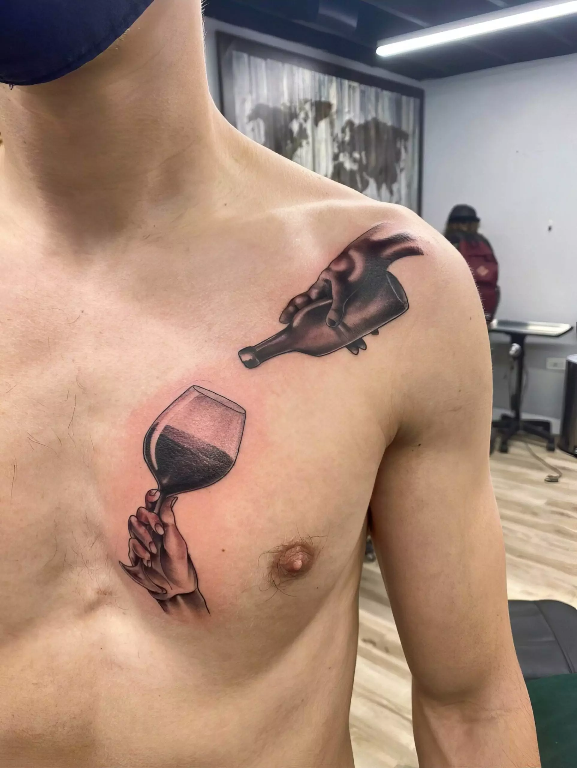 A person with a tattoo on their chest depicting a hand holding a wine glass and another hand pouring wine from a bottle into it.