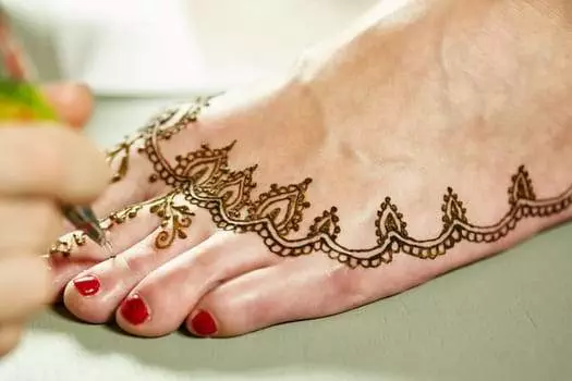 A person is applying intricate henna designs on a foot with red-painted toenails.